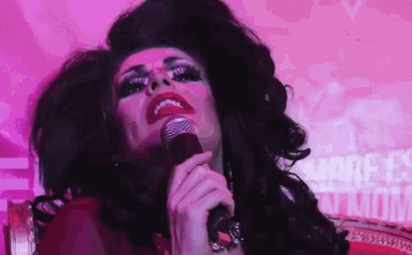 a drag queen is singing into a microphone while holding a gun in her hand .