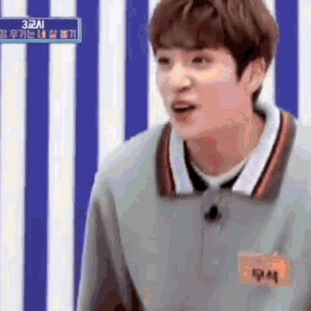 a young man with a name tag on his chest is standing in front of a blue and white striped wall .
