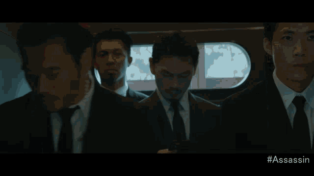 a man in a suit and tie is standing in front of a window with #assassin written on the bottom of the screen