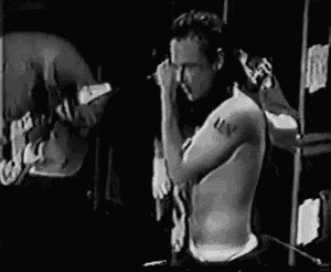 a man without a shirt is singing into a microphone on a stage in a black and white photo .