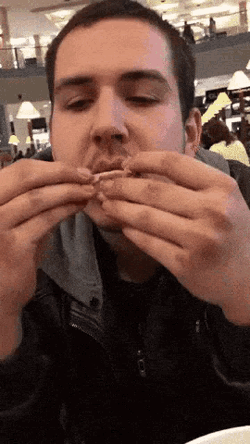 a man in a black jacket is eating a sandwich with his mouth open