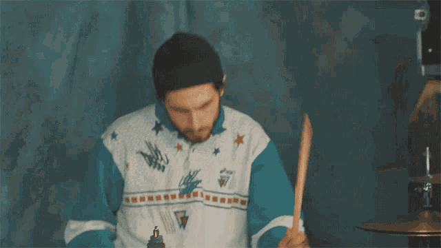a man playing drums wearing a shirt that says asics