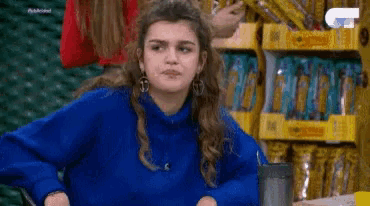 a woman in a blue sweater is sticking her tongue out in front of a shelf of snacks .