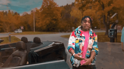 a man in a colorful jacket is standing in front of a car