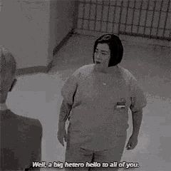a woman in a prison uniform is standing in a hallway and talking to someone .