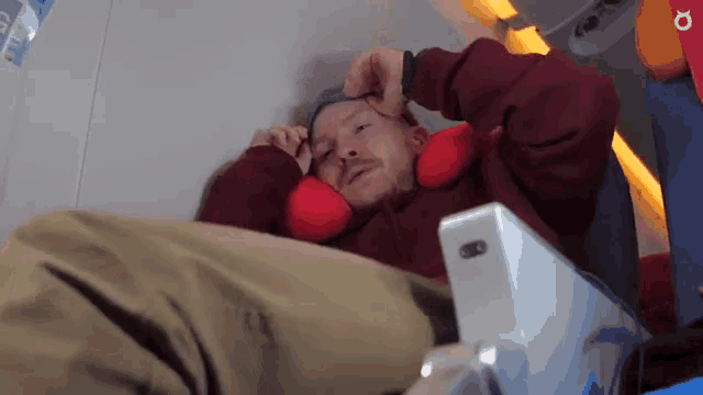a man in a red sweater is laying on an airplane with a red pillow on his head