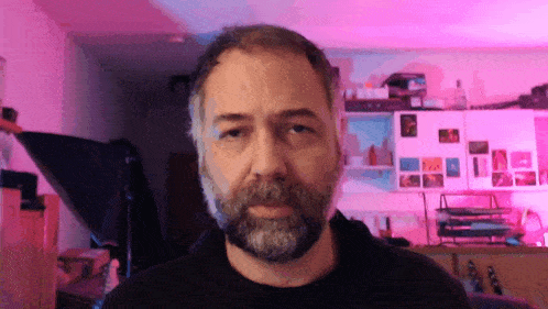 a man with a beard is looking at the camera with a pink light behind him