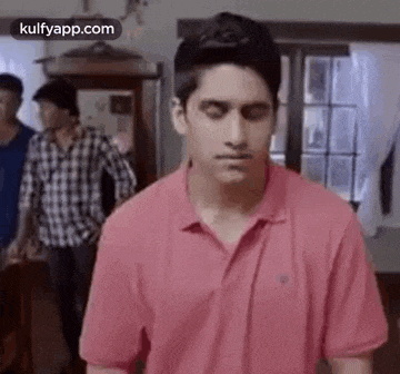 a young man in a pink polo shirt is standing in a living room with his eyes closed .