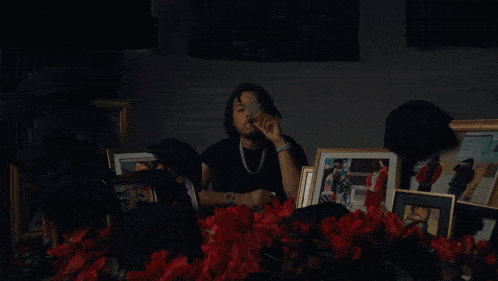 a man smoking a cigarette in front of a table full of pictures