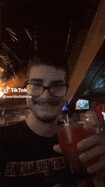 a man wearing glasses is holding a glass of red liquid with a straw and a tiktok watermark