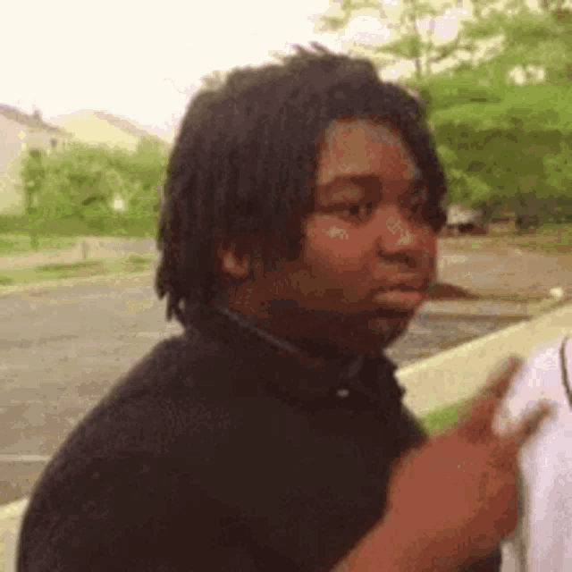 a man with dreadlocks is pointing at something while standing next to another man in a parking lot .