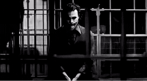 a black and white photo of the joker pointing a gun .