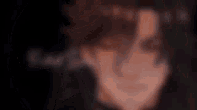 a close up of a person 's face with a black background and a blurred background .