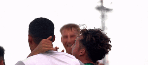 a group of men are hugging each other and one of them is wearing a green shirt