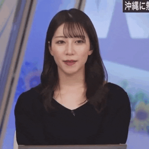 a woman in a black shirt is sitting in front of a sign that says " okinawa "