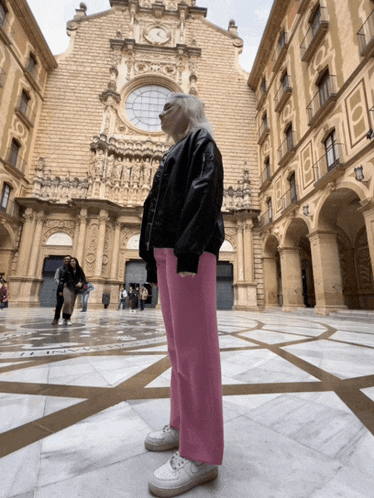 a woman in pink pants stands in front of a building