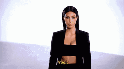 a woman in a black jacket and crop top is standing in front of a white background and making a funny face .