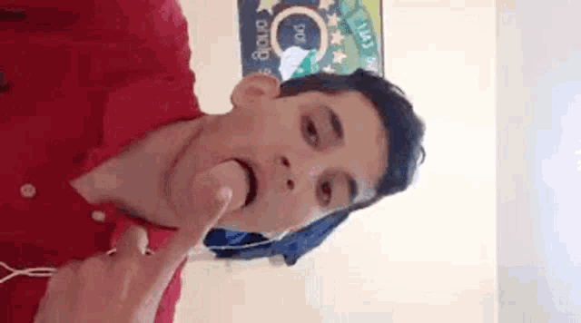 a young man in a red shirt is sticking his tongue out while wearing headphones .