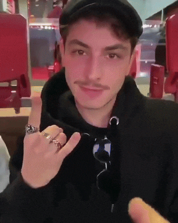 a man wearing a black hat and a black hoodie is making a devil horn sign