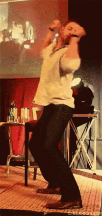 a man in a white shirt is dancing on a stage in front of a projector screen