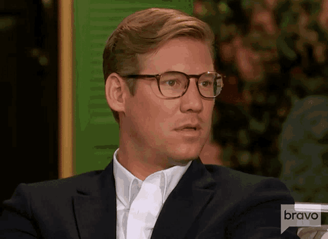 a man wearing glasses and a suit is sitting in front of a screen that says bravo
