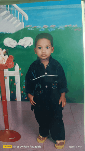 a young boy is standing in front of a painting that says realme shot by ram pagadala