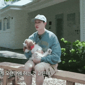 a man sitting on a bench holding a small dog with korean writing on the bottom