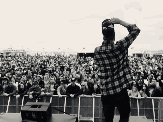 a man in a plaid shirt stands in front of a crowd at a festival