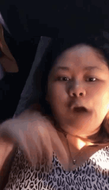 a woman in a leopard print top is making a funny face while laying on a bed .