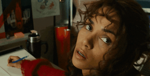 a woman with curly hair is writing on a piece of paper with a blue pen