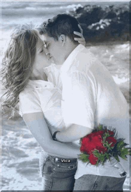 a man holding a bouquet of red roses is kissing a woman on the beach