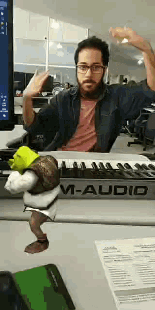 a man is sitting at a desk with a keyboard and a shrek toy on it .