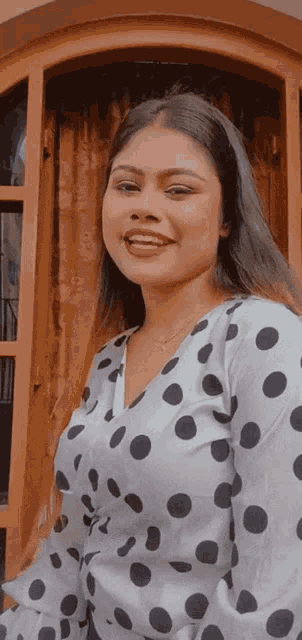 a woman in a polka dot shirt is smiling in front of a window
