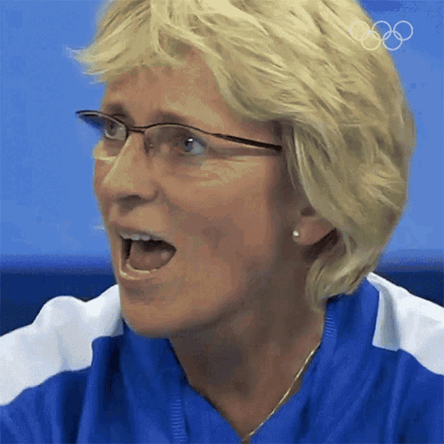 a close up of a woman wearing glasses and a blue shirt with the olympic rings on it