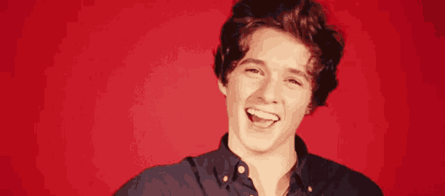 a young man with braces on his teeth is laughing with his mouth open in front of a red background .