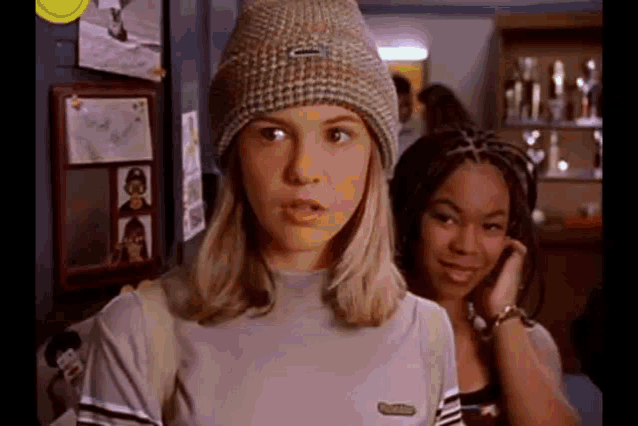 a girl wearing a beanie and a t-shirt is standing next to another girl .