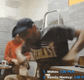 a man wearing a shirt that says " mekes " is sitting at a table
