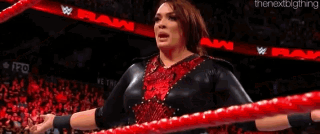 a woman in a black and red outfit is in a wrestling ring