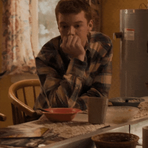a man in a plaid shirt sits at a table with a bowl of soup