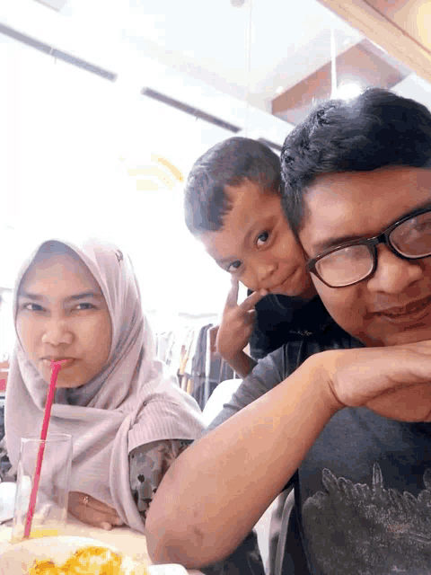 a man wearing glasses holds a child while a woman drinks through a red straw
