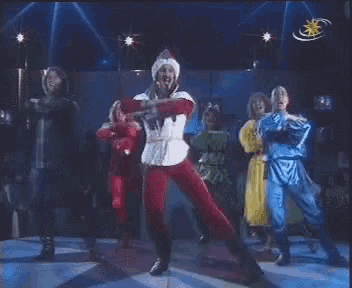 a group of people are dancing on a stage with a star on the bottom left
