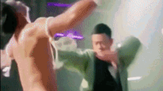a man without a shirt is standing next to another man in a green suit .