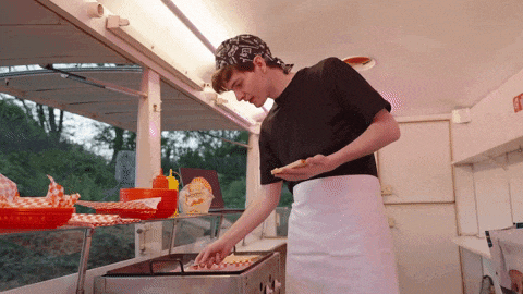 a man in a black shirt and white apron is cooking a pizza