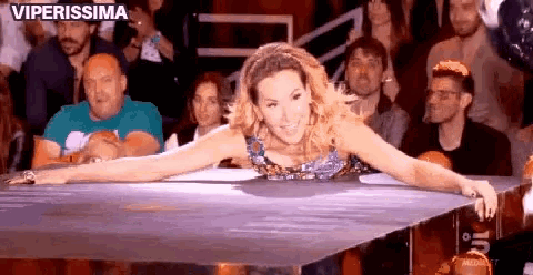 a woman is leaning over a table in front of a crowd with the words viperissima written on the bottom