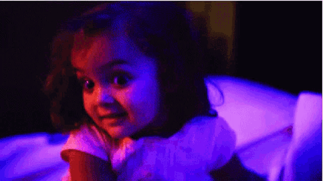 a little girl is sitting in front of a blue light