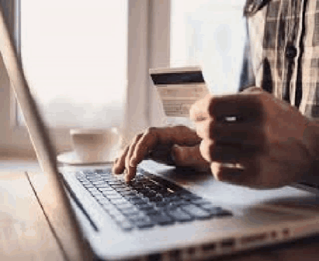 a man is holding a credit card while typing on a laptop .