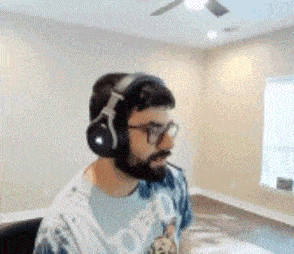 a man with a beard wearing headphones and glasses is sitting in a room .