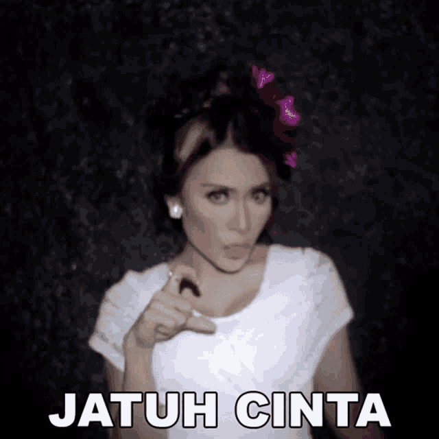 a woman with a flower in her hair is pointing at the camera and the words jatuh cinta are below her