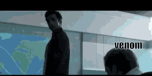 a man in a suit is standing in front of a large screen with the word venom on it .