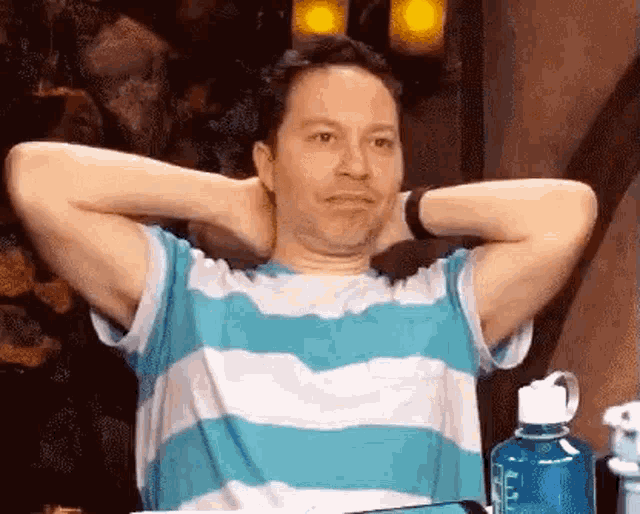 a man in a blue and white striped shirt with his hands behind his head .